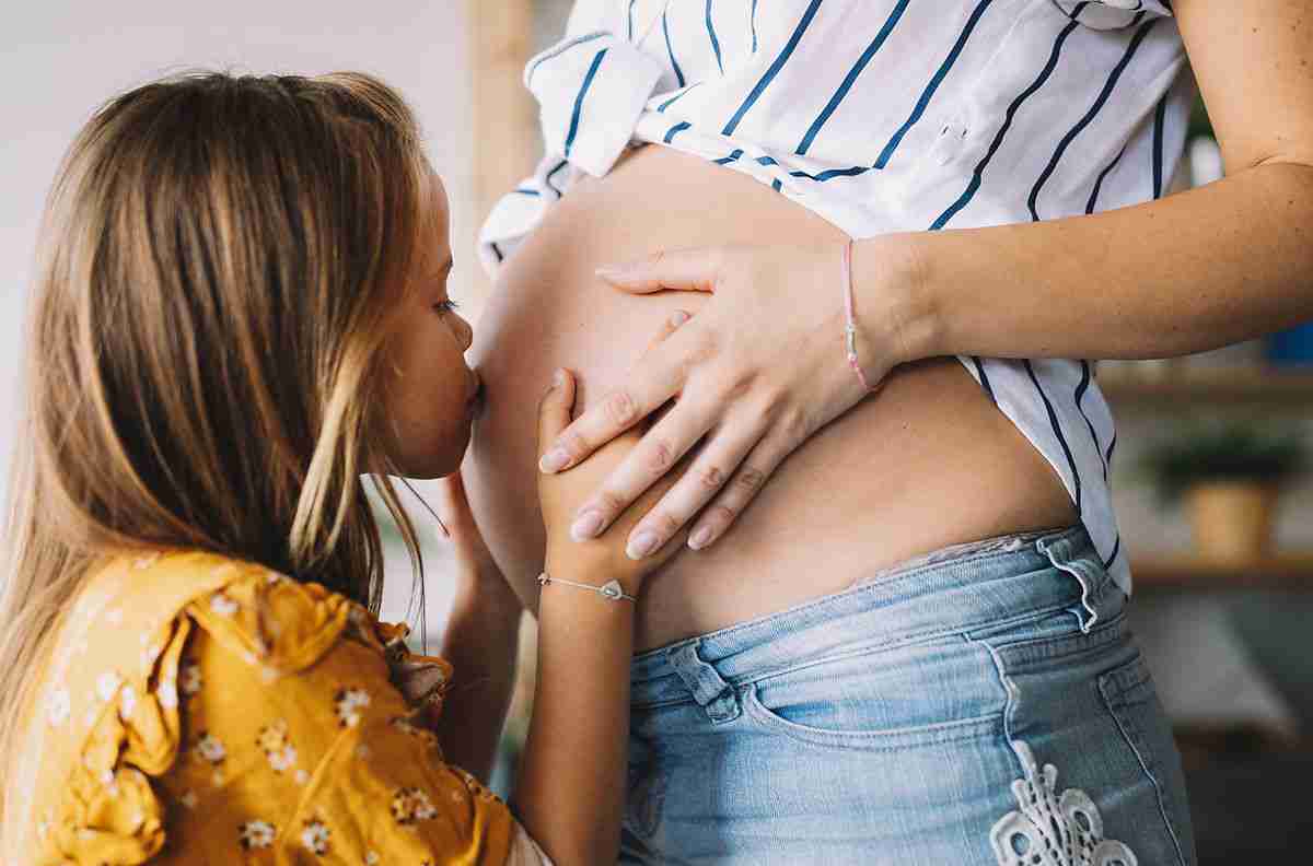 young girl kissing mom's pregnant belly